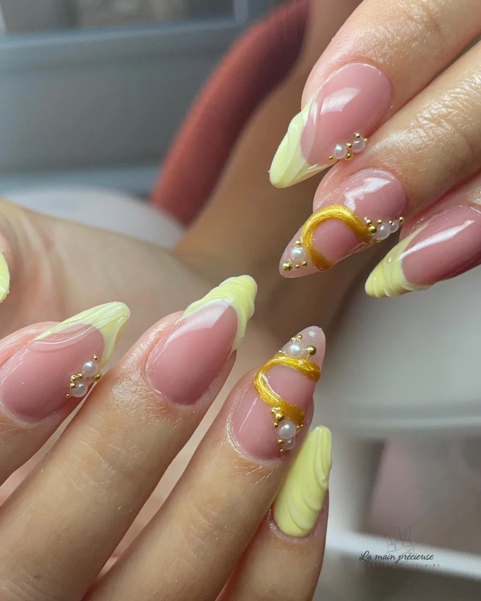 Manucure jaune pastel ornée de perles et d'ornements dorés